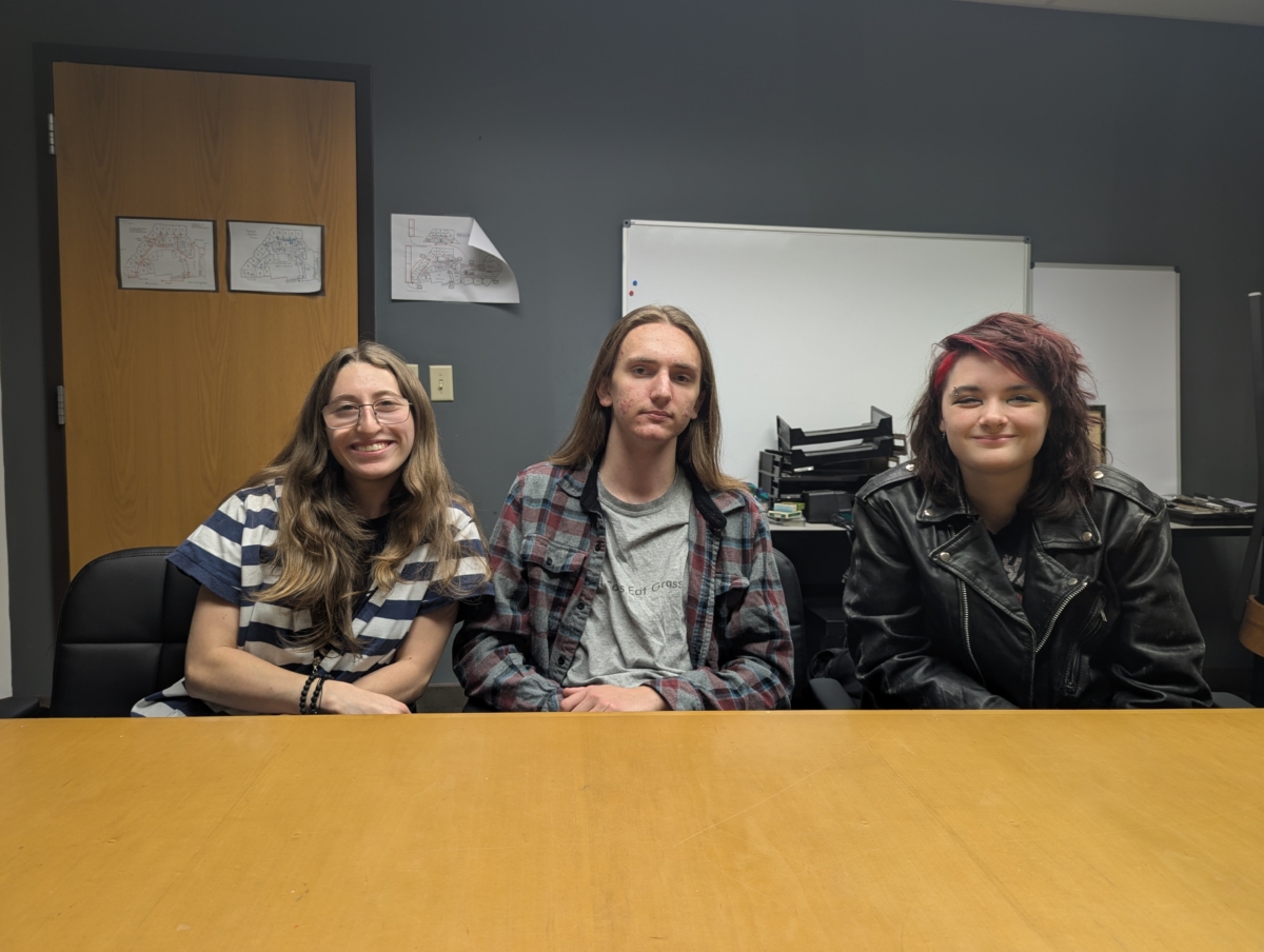 Three students smiling for a photo. On the left, Sadie is wearing glasses and a striped shirt. In the middle, Axel is wearing a gray shirt and a red and gray flannel. On the right, Jules is wearing a leather jacket.
