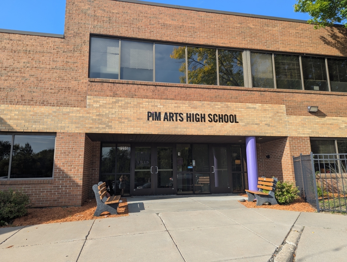 The outside of the PiM Arts High School building. The building is made of brick and has two benches outside the doors.