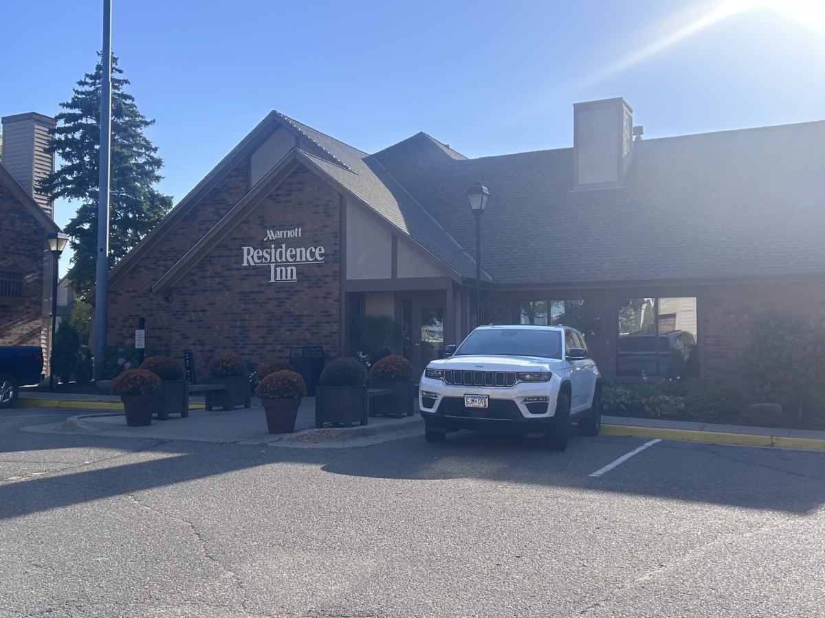 A brown brick building with the words "Marriott Residence Inn" on the front in white letters sits under a blue style. A white car is in front of the building.
