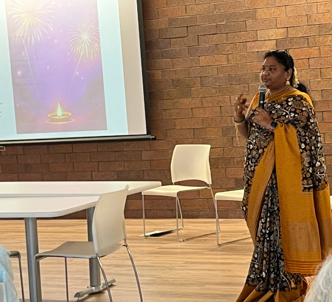 woman in floral dress and yellow gold sari stands in front of slide showing fireworks
