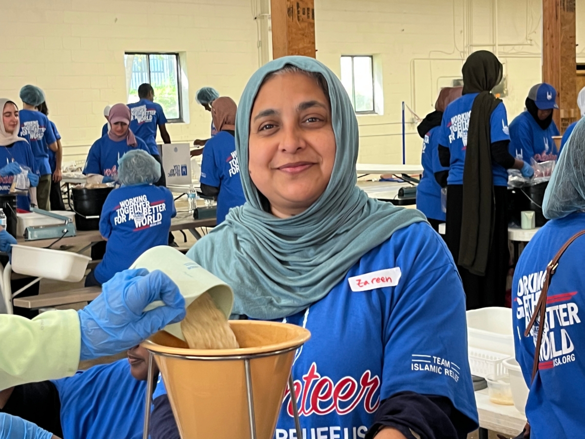 woman in green hijab smiles behind funnel as hand pours rice from cup