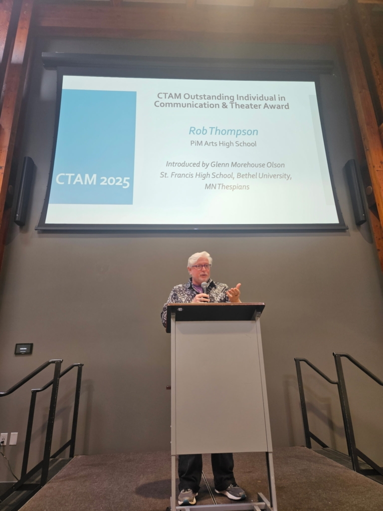 Rob Thompson stands at a podium and accepts the CTAM Outstanding Individual in Communication & Theater Award on Sept. 19, 2025. A projected screen with Rob's name is behind him.