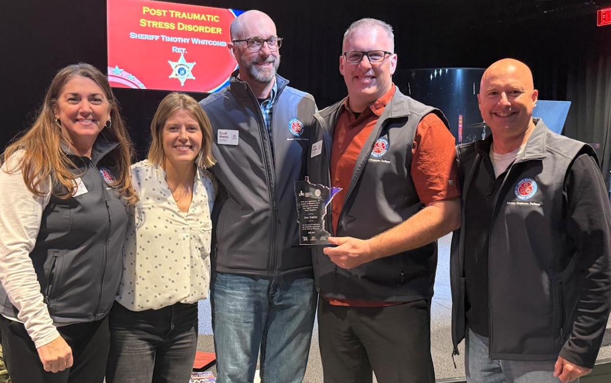 Smiling people surround Lt. Jess Irmiter, second from left, wearing an orange shirt with a vest.