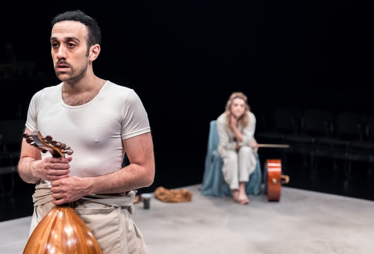 Actor George Abud holds an oud in the foreground while Sydney Shepherd, seated with a cello beside her, watches in the background during a performance of “The Ruins: A Play Through Music” at Guthrie Theater’s Dowling Studio.
