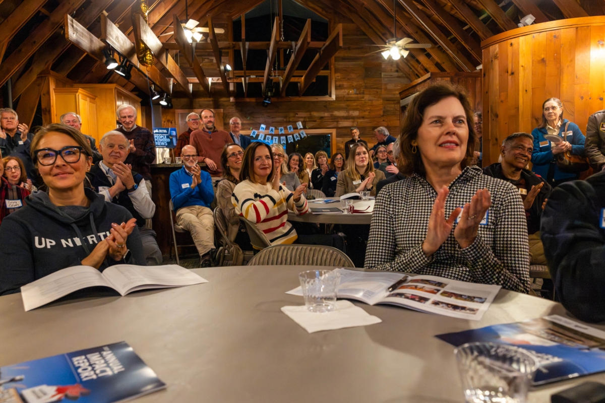 crowd of people applauding in interior with exposed rafters, Happy Birthday sign in background