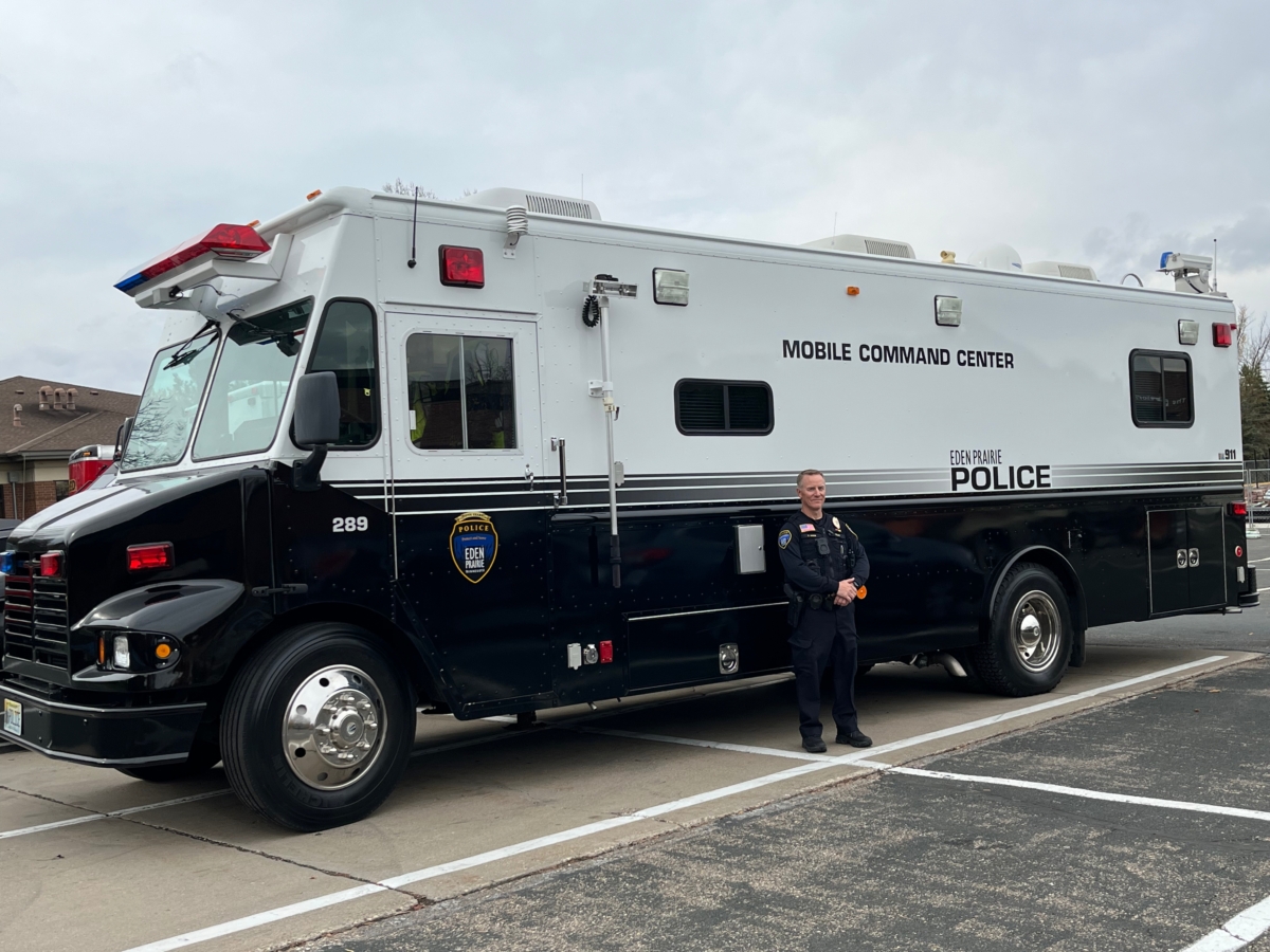 uniformed police officer standing outside large Mobile Command Unit vehicle