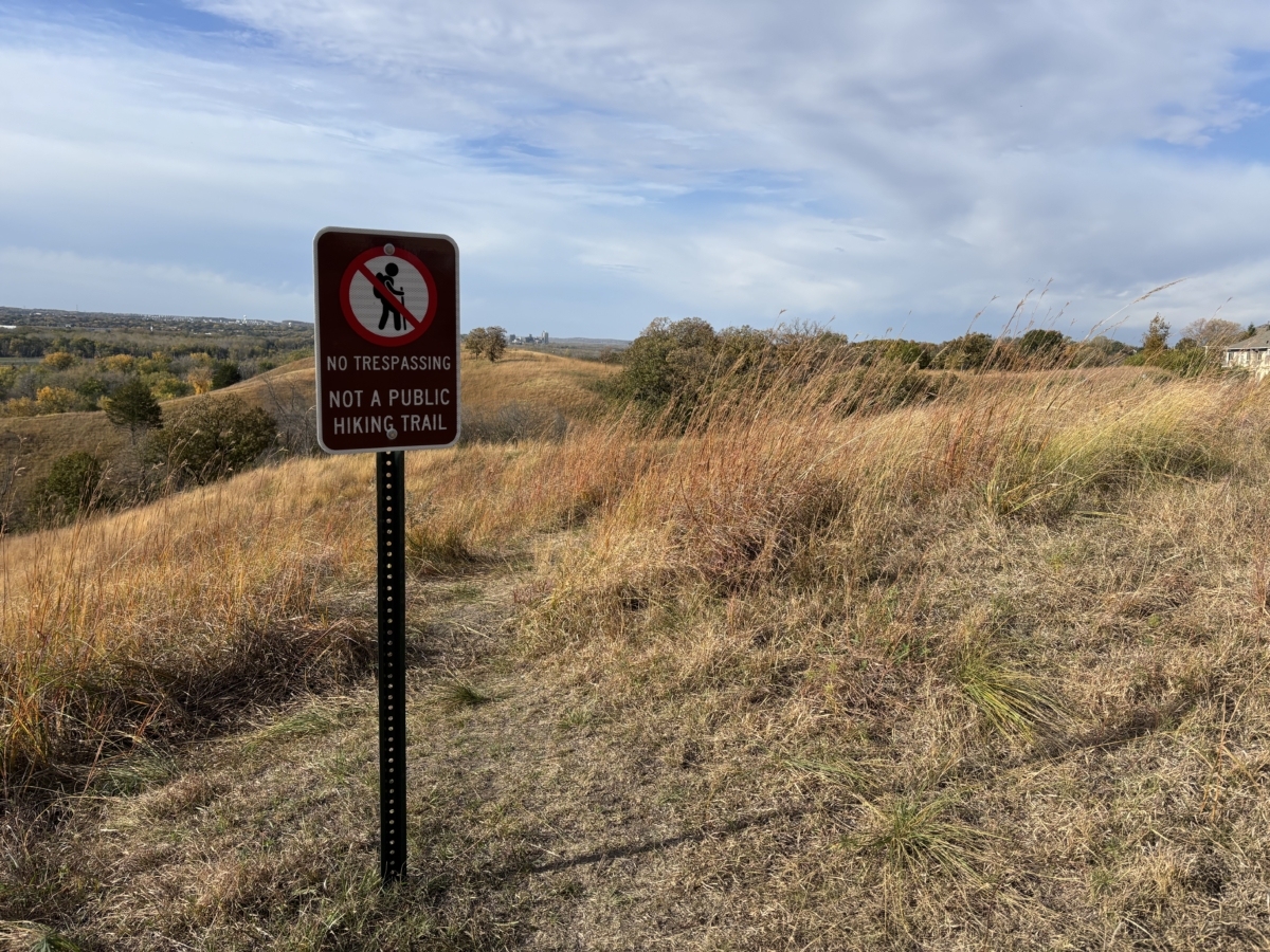 rolling hills of native prairie in background with a sign that says no trespassing, not a public hiking trail in the foreground