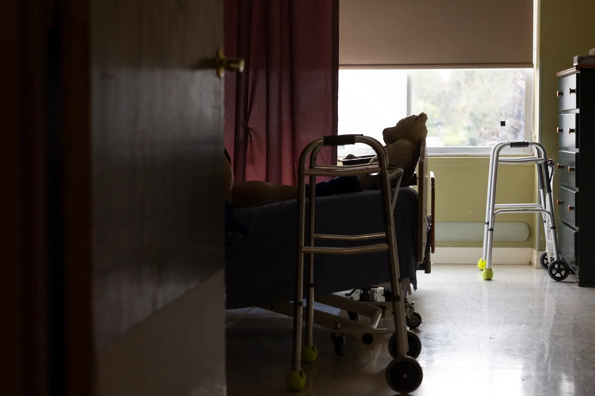 A teddy bear sits at the feet of a resident at Maplewood Rehabilitation Center on Tuesday, Sept. 30, 2025, in Maplewood, Minnesota. Photo by Ellen Schmidt/MinnPost/CatchLight