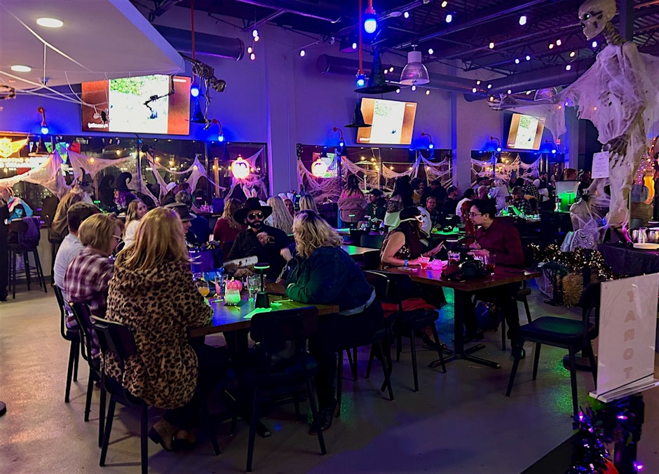 A crowd sitting at tables with Halloween decorations throughout the room