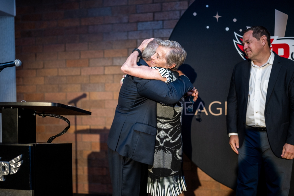 Sen. Steve Cwodzinski and Linda Wallenberg hug onstage at the Eagle Excellence Showcase. Superintendent Josh Swanson looks at them with a smile.