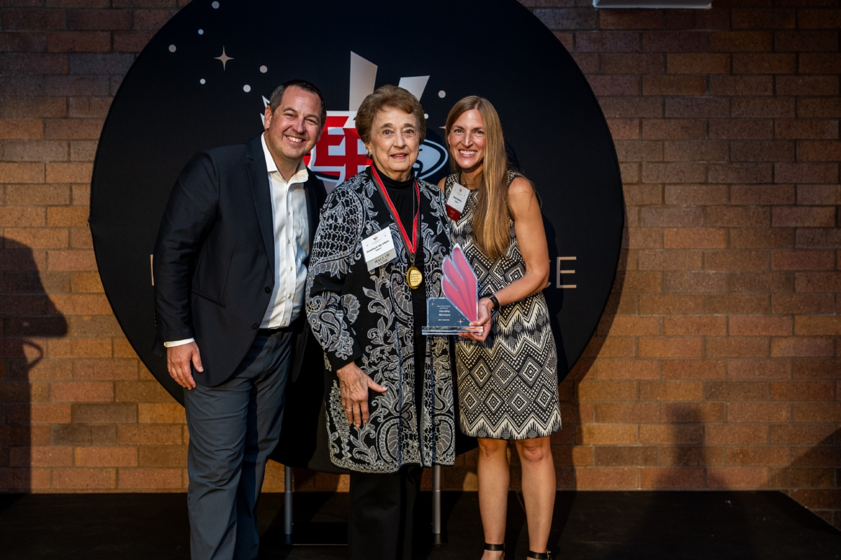 Josh Swanson, Dorothy McIntyre and Molly Malone smile for a picture with McIntyre's Hall of Fame trophy. McIntyre is also wearing a medal around her neck.