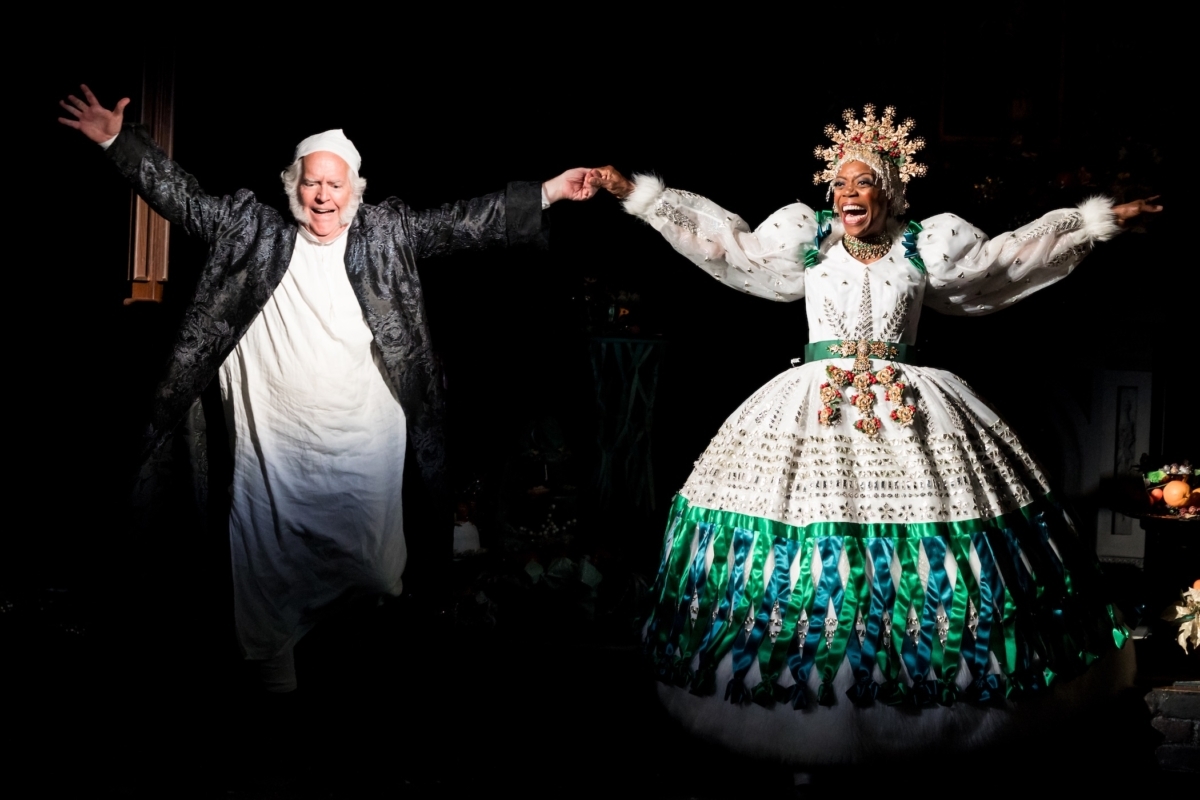 David Beach as Ebenezer Scrooge and Regina Marie Williams as the Ghost of Christmas Present hold hands and celebrate joyfully onstage in the Guthrie Theater’s production of “A Christmas Carol.”
