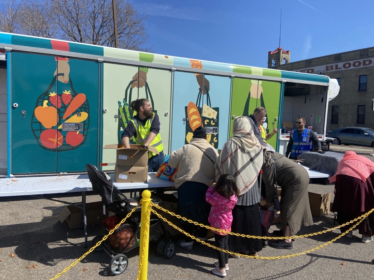 Volunteers help families collect food from a Second Harvest Heartland mobile distribution truck decorated with produce illustrations.