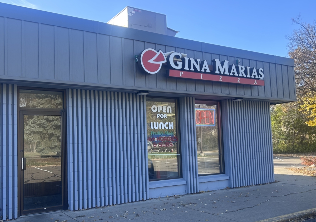 Gina Marias Pizza sits in a gray building. Its window indicates it is open.