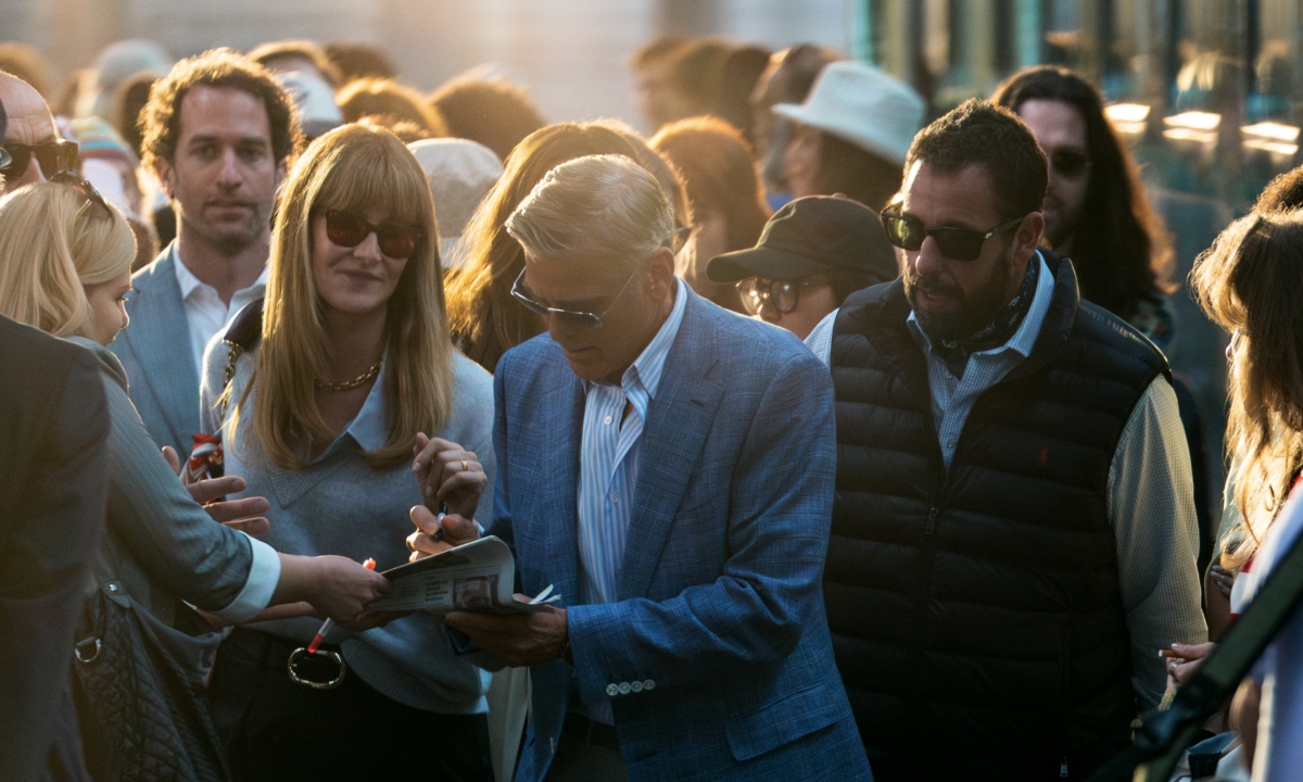 A man is surrounded by fans. He is signing autographs.