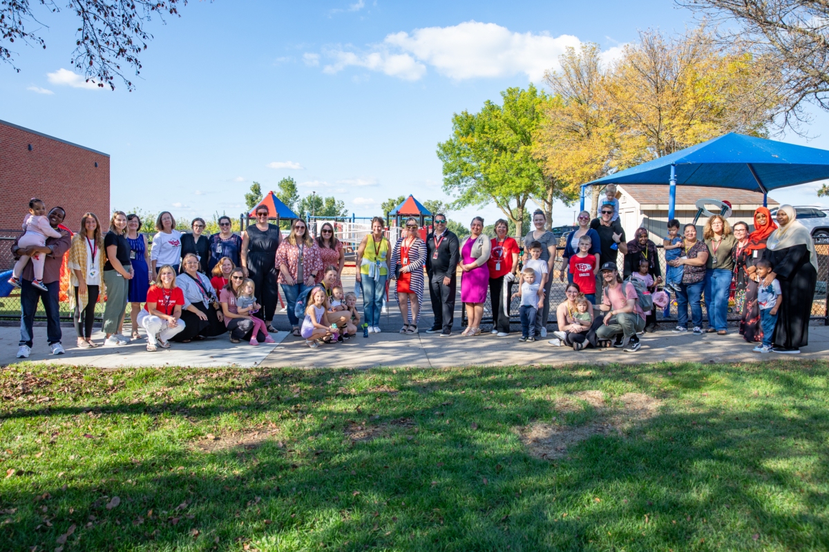 Eden Prairie Schools family and staff stand in a line and smile for a photo in front of the Little Eagles Playground.