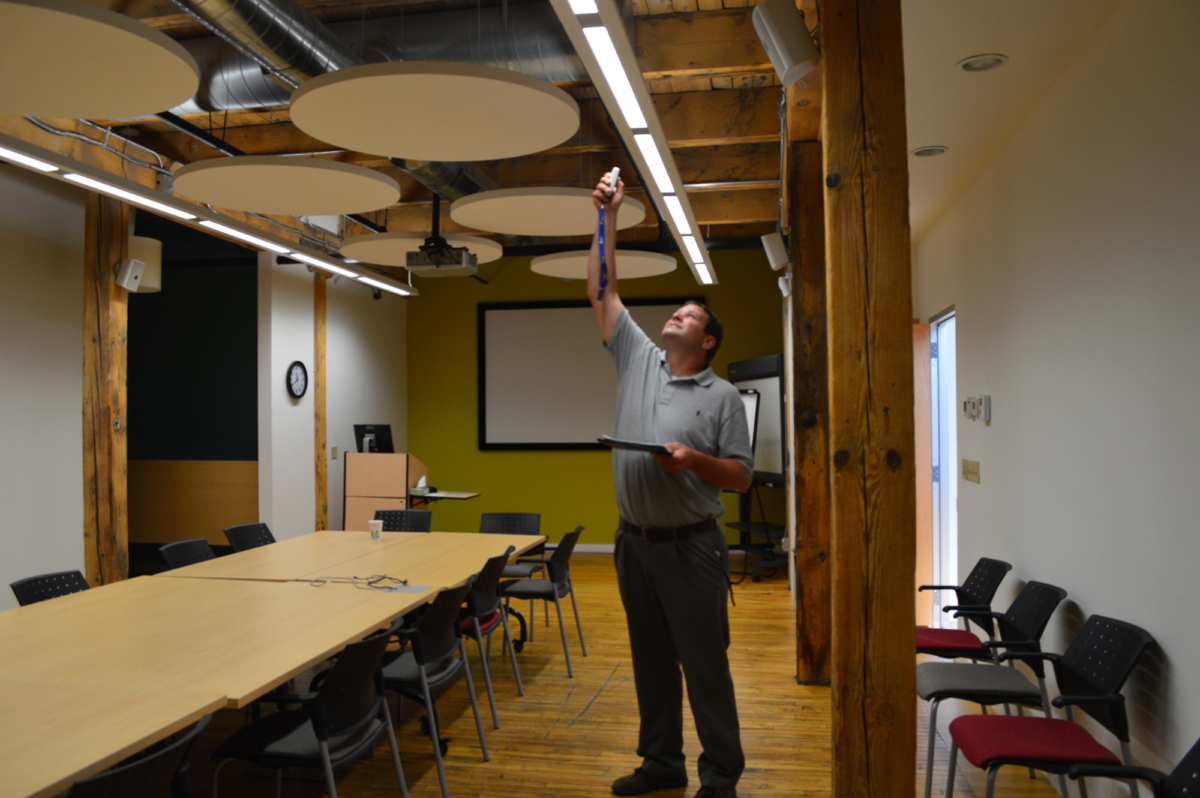 man with clipboard reaching up to assess overhead lighting in conference room