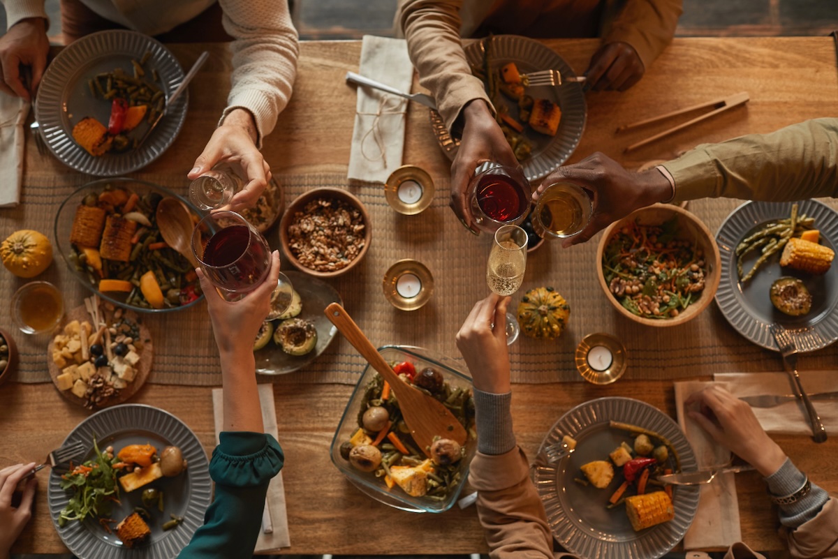A Thanksgiving meal spread with a roasted turkey, vegetables, and seasonal decorations on a dining table, with people gathered in the soft-focus background.
