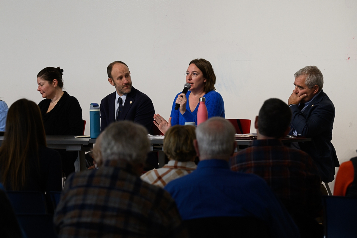 A group of people sit at a banquet table. A woman in a blue shirt is speaking into a microphone
