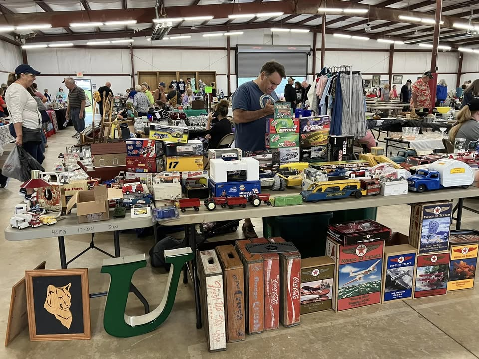 A man shopping in a warehouse setting at a table piled with toys.