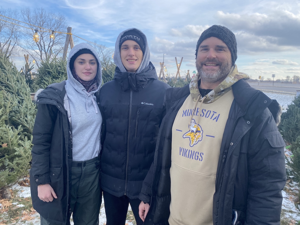 Lilja, Birkir and Kyle Gudmundson stand bundled in winter jackets among rows of Christmas trees at Scouts BSA Troop 695’s lot in Eden Prairie.