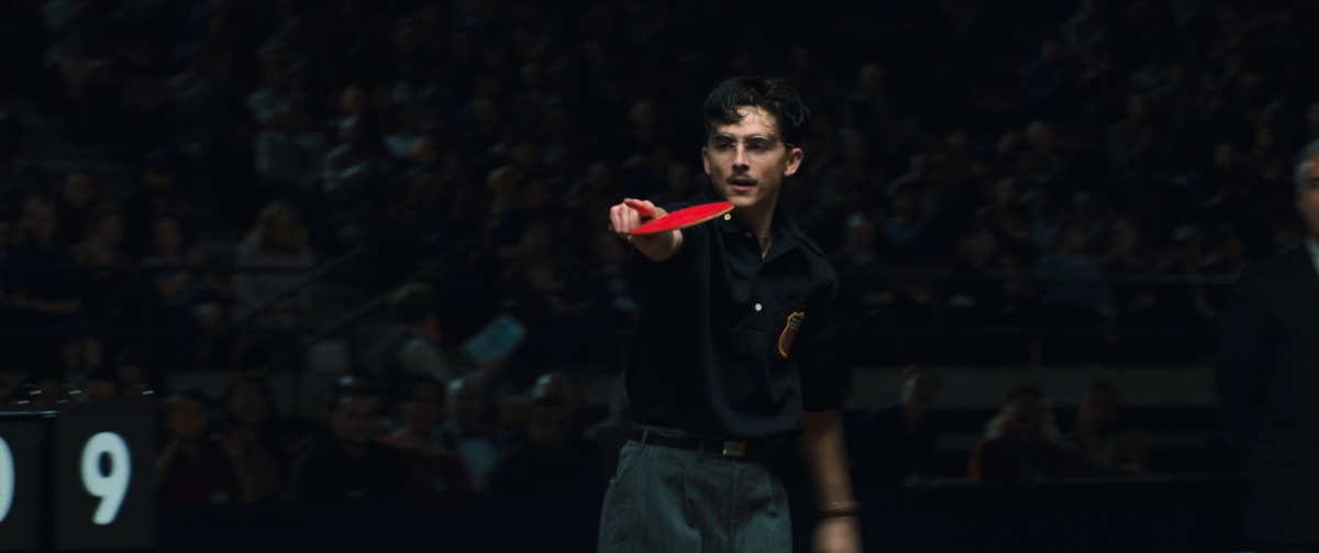A man holds a table tennis paddle, pointing ahead.